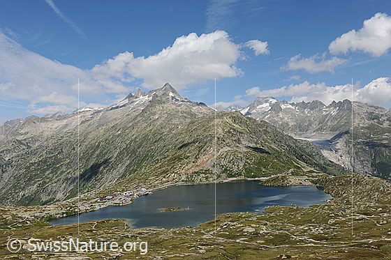 Foto: Grimselpass und Totesee mit Aussicht zu Gärstenhörner und Urner Alpen mit Galenstock, Gross Furkahorn und Klein Furkahorn. Über den Bergen sind Quellwolken zu sehen.