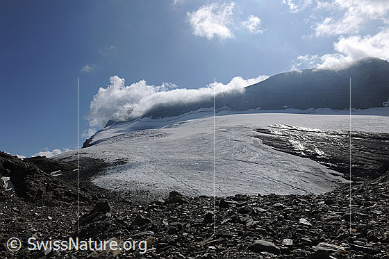 Foto: Chaltwassergletscher und Monte Leone mit Quellwolken. Im Vordergrund ist ein Geröllfeld zu sehen.