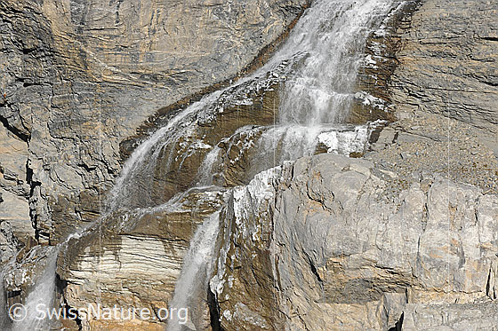 Foto: Vereister Wasserfall. Das Wasser fliesst über die Felsstufen, an welchen sich durch Spritzwasser Vereisungen gebildet haben.