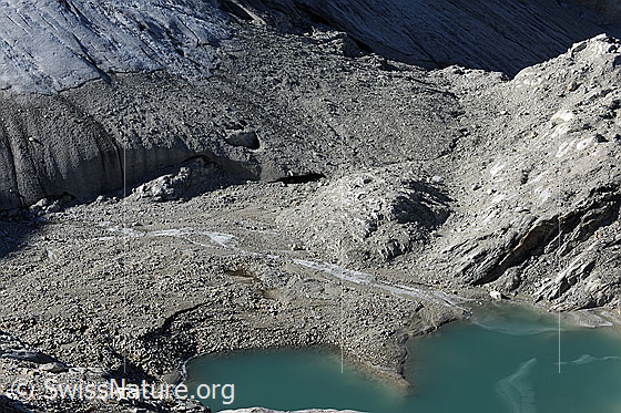 Foto: Brunegggletscher: Zunge, Tor, Gletscherbach und Gletschersee. Auf der Gletscherzunge über dem Gletschertor hat sich Gesteinsschutt abgelagert. Im Gletschersee sind Eisreste zu sehen.