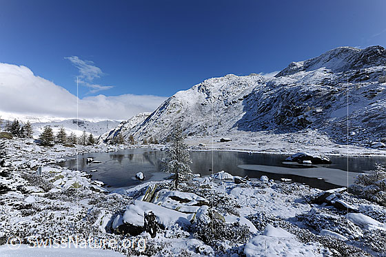 Foto: Märchenlandschaft Mässersee nach erstem Schnee im Hebst. Im Schwarzeis des Bergsees spiegeln sich die Lärchen.