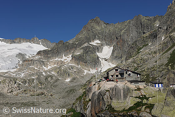 Foto: Albert-Heim-Hütte. Die Berghütte befindet sich auf einem Felskopf. Dahinter sind das Gletschhorn und in seinen Felswänden die Reste des Sunniggletschers zu sehen.