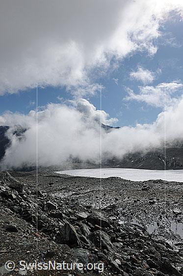 Foto: Wolkenstimmung über dem Gletscher. Blick über den mit Geröll bedeckten Gletscherrand (= Obermoräne) auf den Schwarzberggletscher. Die Restbewölkung reisst auf und es bilden sich Quellwolken.
