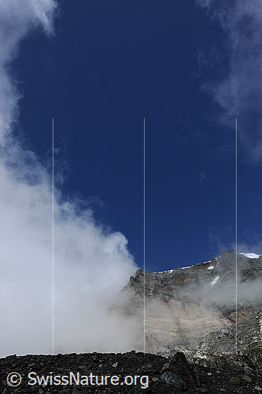 Foto: Wolkenstimmung und Felswand. An den mächtigen Wänden von Strahlhorn und Fluchthorn ziehen Wolkenfetzen vorübe Im Vordergrund sind Gletschereis und loses Gestein der Seitenmoräne des Schwarzberggletschers zu sehen.