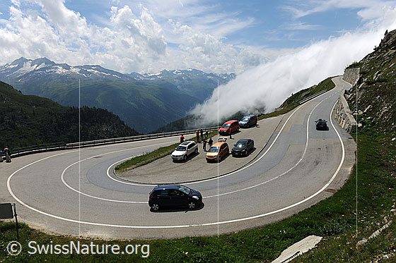 Foto: Mobilität: Autoverkehr auf Passstrasse Richtung Grimselpass mit Kurve und Parkplatz. Im Hintergrund ist die Wolkenwalze der Grimselschlange (Wetterphänomen) zu sehen.