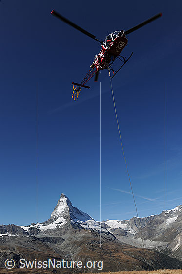 Foto: Helikopter vor Bergkulisse mit Matterhorn. Das Fluggerät steht für eine Gebirgsbaustelle im Einsatz.