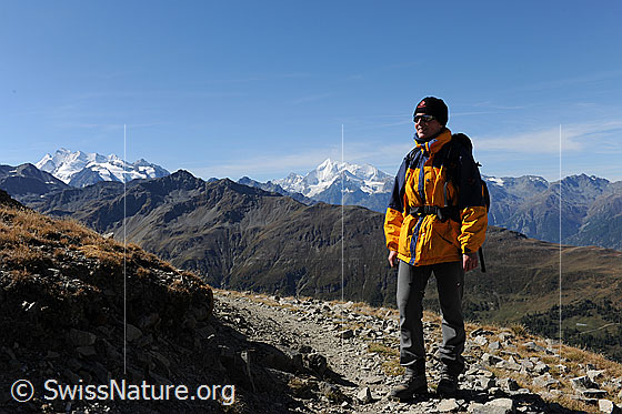 Foto: Wandern im Wallis. Die Wanderin ist auf einem Bergweg unterwegs. Im Hintergrund sind Mischabel und Weisshorn zu sehen.
