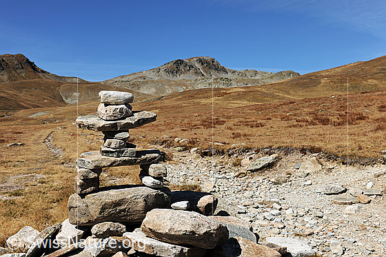Foto: Kunstvoll aufgeschichteter Steinmann als Wegmarkierung auf Bergweg in herbstlicher Berglandschaft.