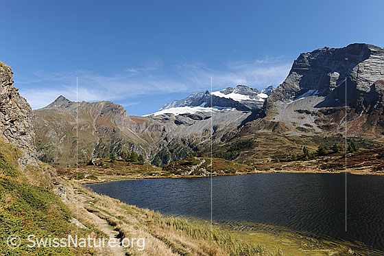 Foto: Wasenhorn, Monte Leone und Hübschhorn davor der Hopschusee. Ein Bergweg führt dem Seeufer entlang.