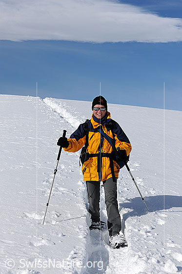 Foto: Schneeschuhläuferin auf Schneeschuhtour an einem sonnigen Wintertag. Am blauen Himmel ist ein Wolkenfeld zu sehen.