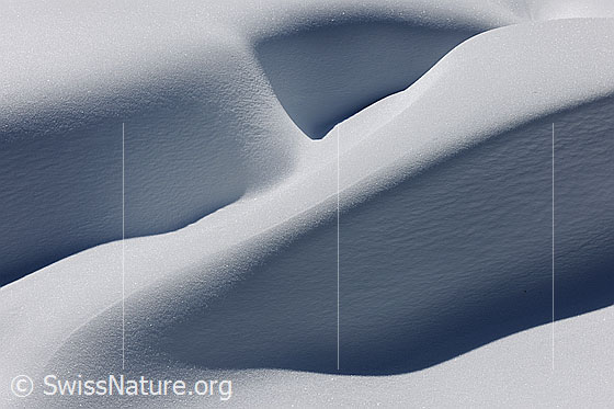 Foto: Schatten und Formen in der Natur. Unberührte, kunstvoll geformte Schneeverwehung mit Licht und Schatten.