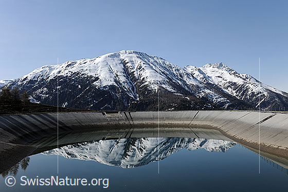Foto: Spiegelung der Berglandschaft in einem Ausgleichsbecken eines Wasserkraftwerks (erneuerbare Energie).