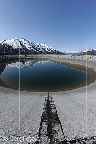Foto: Ausgleichsbecken (Wasserkraft) mit Spiegelung der Berge im ruhigen Wasser.