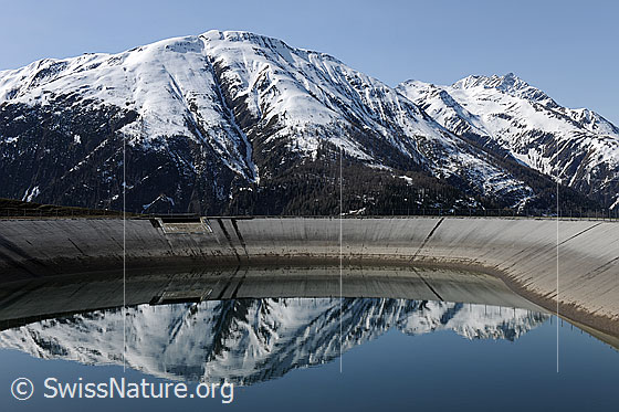 Foto: Verschneite Berge mit Spiegelung in Ausgleichsbecken (Wasserkraft/erneuerbare Energie).