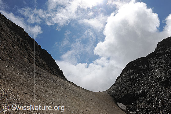 Foto: Übergang (Sattel) in karger Berglandschaft mit Quellwolke im Hintergrund. Die Berghänge sind mit feinem Geröll bedeckt.