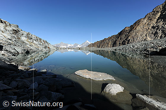 Foto: Am Ufer des Alphubelsee. Blick über die spiegelnde Wasserfläche zu Zinalrothorn und Weisshorn. Die Spiegelung der Berglandschaft mit Gletscherschliff und Felsgrat lassen interessante Formen und Muster entstehen.