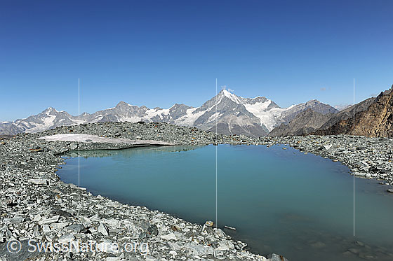 Foto: Bergsee im Hochgebirge. Der See liegt in einem flachen Geröllfeld mit Ausblick zu den Walliser Alpen mit Weisshorn.