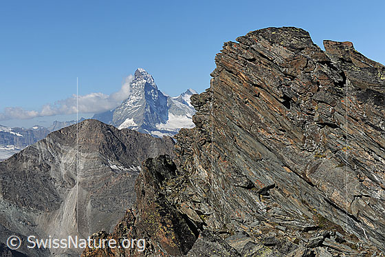 Foto: Oberrothorn und Matterhorn. Im Vordergrund ist ein brüchiger Felsgrat zu sehen. Ein Wolkenband erstreckt sich über die Berggipfel und staut sich am Matterhorn.