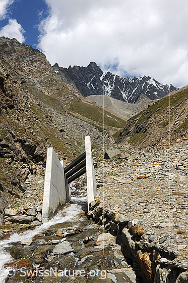 Foto: Durchlass für Bergbach in Lawinenschutzbau. Im Hintergrund ist das Täschhorn mit Quellwolke und die Moräne des Weingartengletschers zu sehen.