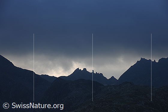 Foto: Felstürme in einer Bergkette, welche als Silhouette zu sehen ist. Darüber liegen dunkle Regenwolken und verleihen der Berglandschaft eine mystische Stimmung.