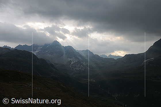 Foto: Sonnenstrahlen brechen durch die dunkle Wolkendecke über der Berglandschaft (Wolkenstimmung während eines Föhnsturms).