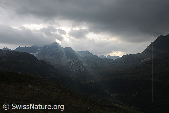 Foto: Wolkenstimmung während eines Föhnsturms. Lichtstrahlen brechen durch die dunkle Wolkendecke über der Berglandschaft.