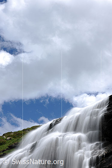 Foto: Erfrischender Wasserfall (Langzeitbelichtung). Zahlreiche Wasserstrahlen strömen über mehrere Felsstufen. Am Himmel ist Quellbewölkung zu sehen.