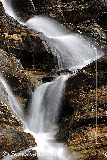 Foto: Kleine Wasserfälle über Felsbänder aus Bündner Schiefer. Langzeitbelichtung.
Hören Sie das erfrischende Rauschen des Wasserfalls?