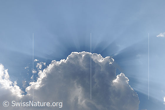 Foto: Wolkenstimmung mit Quellwolke und Sonnenstrahlen/Lichtstrahlen. Mächtige Quellwolke mit hellem Rand und Sonnenstrahlen, welche über den blauen Himmel erstrahlen.