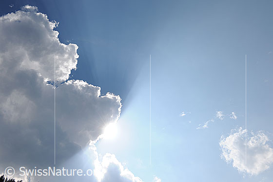 Foto: Lichtstimmung mit Sonne und Wolke. Sonnenstrahlen brechen durch die dunkle Cumuluswolke, welche am Rand hell erleuchtet ist.