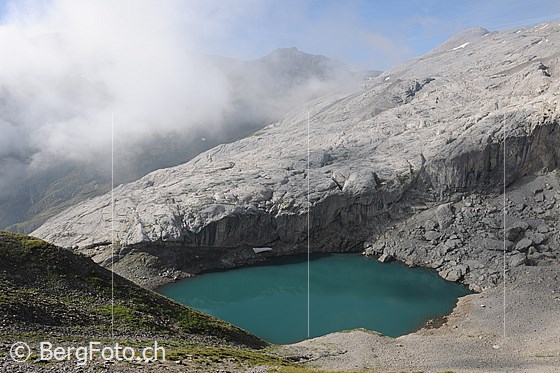 Foto: Lac de Ténéhet mit türkisfarbenem Wasser und Wolkenstimmung. Ein heller Felsriegel begrenzt die kleine Mulde, in welcher der Bergsee eingebettet liegt.