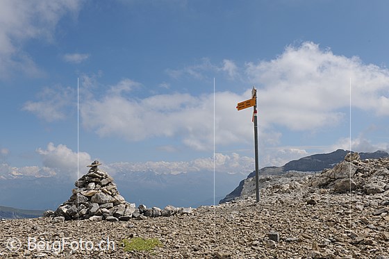 Foto: Schnidejoch.
Am Übergang stehen Steinmann und Wegweiser und über dem Wallis sind Quellwolken zu sehen.