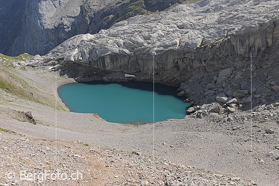 Foto: Tiefblick auf den Lac de Ténéhet umgeben von Geröllhängen und einem Felsriegel. Das Wasser des Bergsees hat die Farbe türkis.