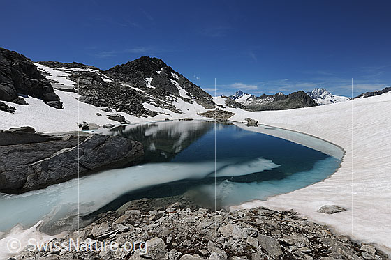 Foto: Felsblock und langezogene Eisscholle in Bergsee.