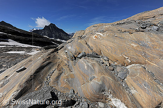 Foto: Marmorierter Gletscherschliff vor pyramidenförmigem Berg. Mit Wolkenfahne am Gipfel des Bergs.
