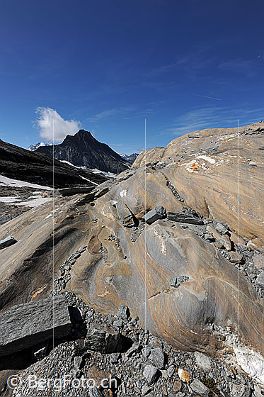 Foto: Marmorierter Gletscherschliff vor pyramidenförmigem Berg. Mit Wolkenfahne am Gipfel des Bergs.