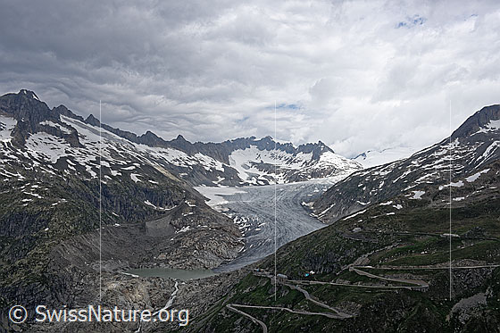 Foto: Berglandschaft mit Rhonegletscher, Gletschersee und Ursprung der Rhone. Die Gletscherzunge mündet in den See. Rechts im Bild ziehen sich die Kurven der Passstrasse zum Furkapass hoch. Im Hintergrund sind die Gärstenhörner und die Gelmerhörner zu sehen.
