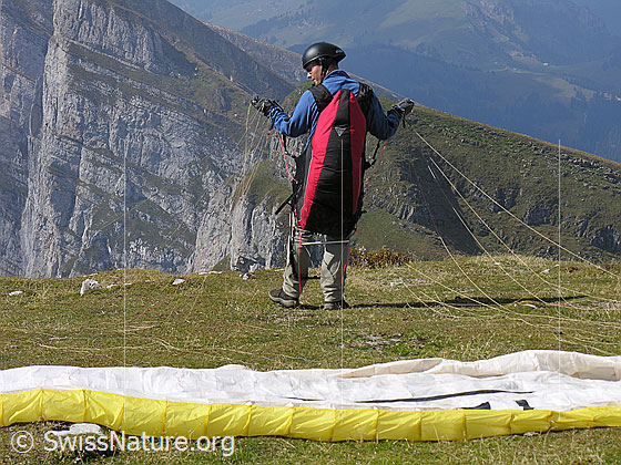 Foto: Gleitschirmpilot kurz vor dem Start. Der Gleitschirm ist am Boden ausgebreitet und der Pilot wartet den richtigen Moment ab.