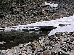 F026003: Geröll und Eis am Ufer eines Bergsees