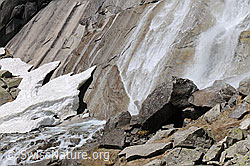 F058317: Schneereste und Wasserfall am Fuss einer Felswand